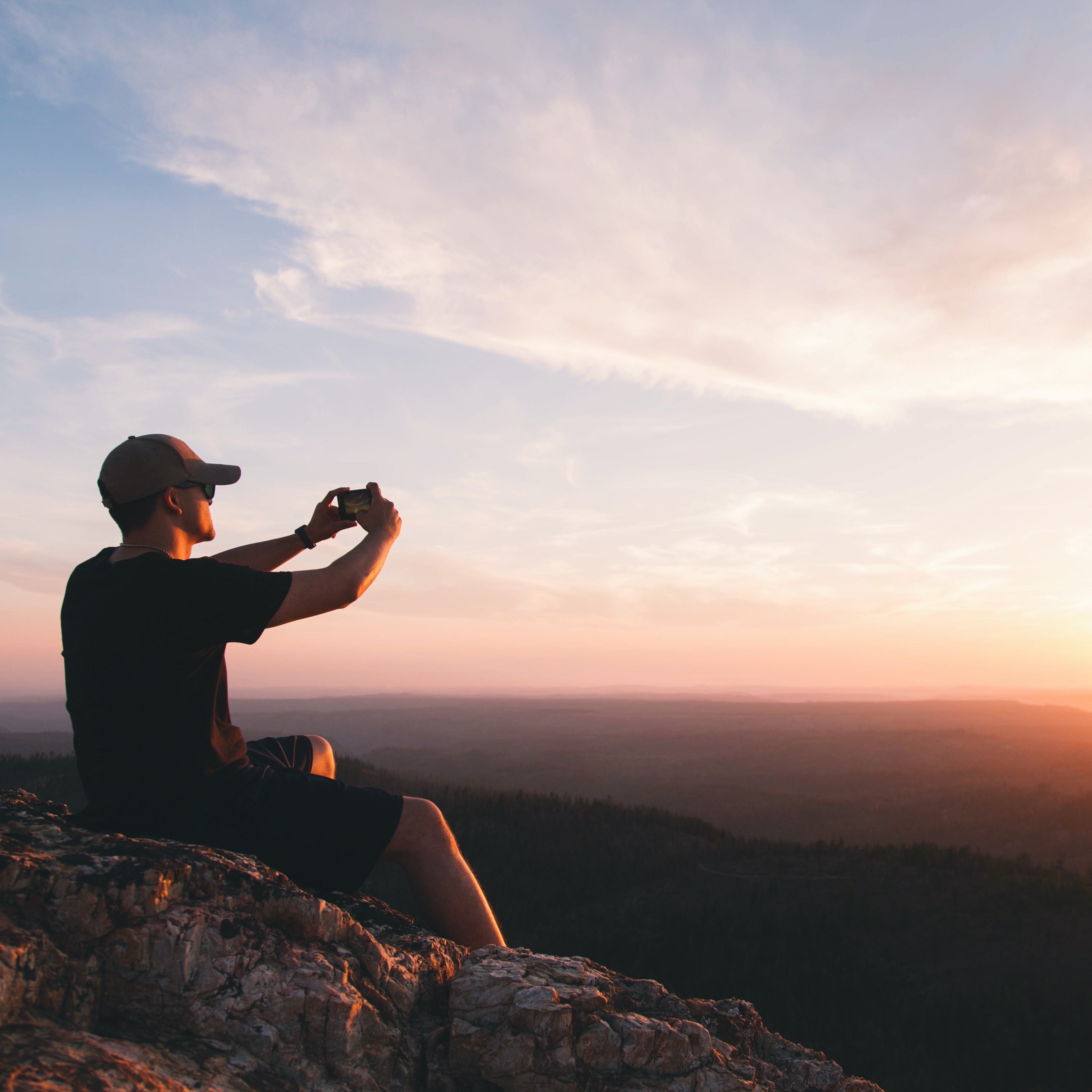 Man Capturing Sunset Photo on Mountain with iPhone