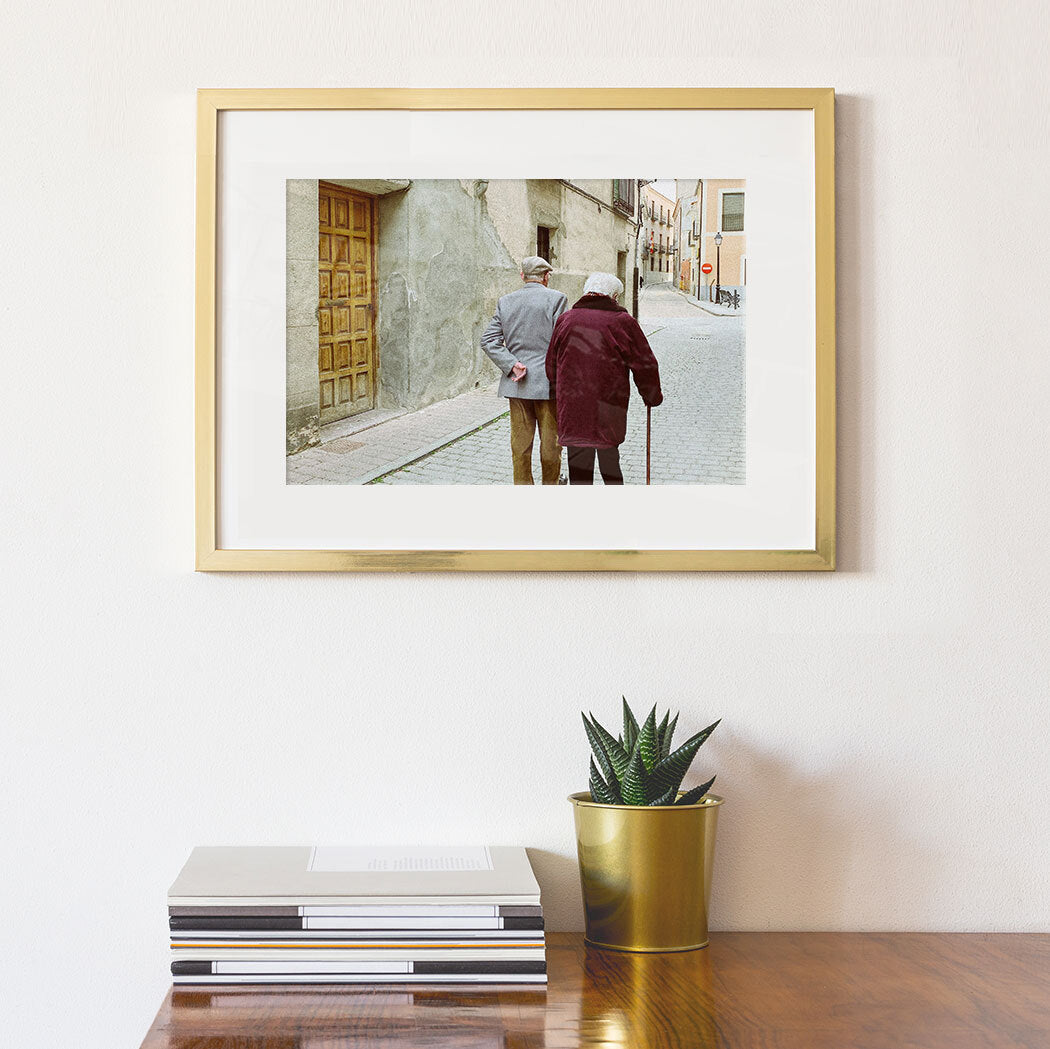 Photo of elderly couple walking, printed and framed in gold, displayed on a wall above a desk