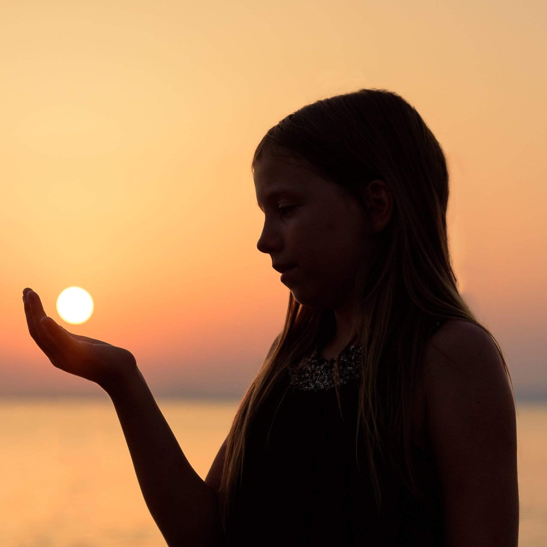 Silhouette of a girl holding the sun in her hand