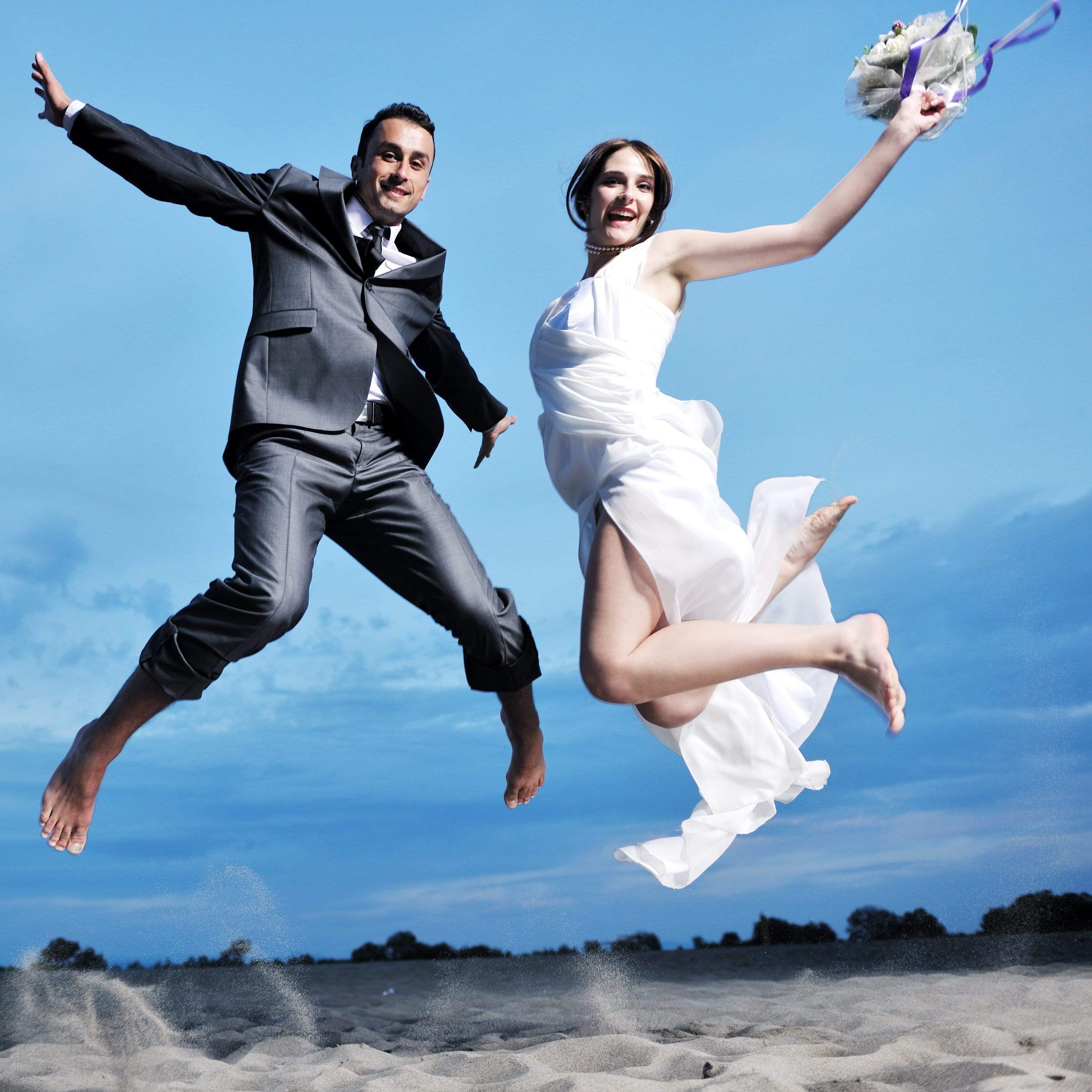 Bride and groom jumping on the beach barefoot in the sand